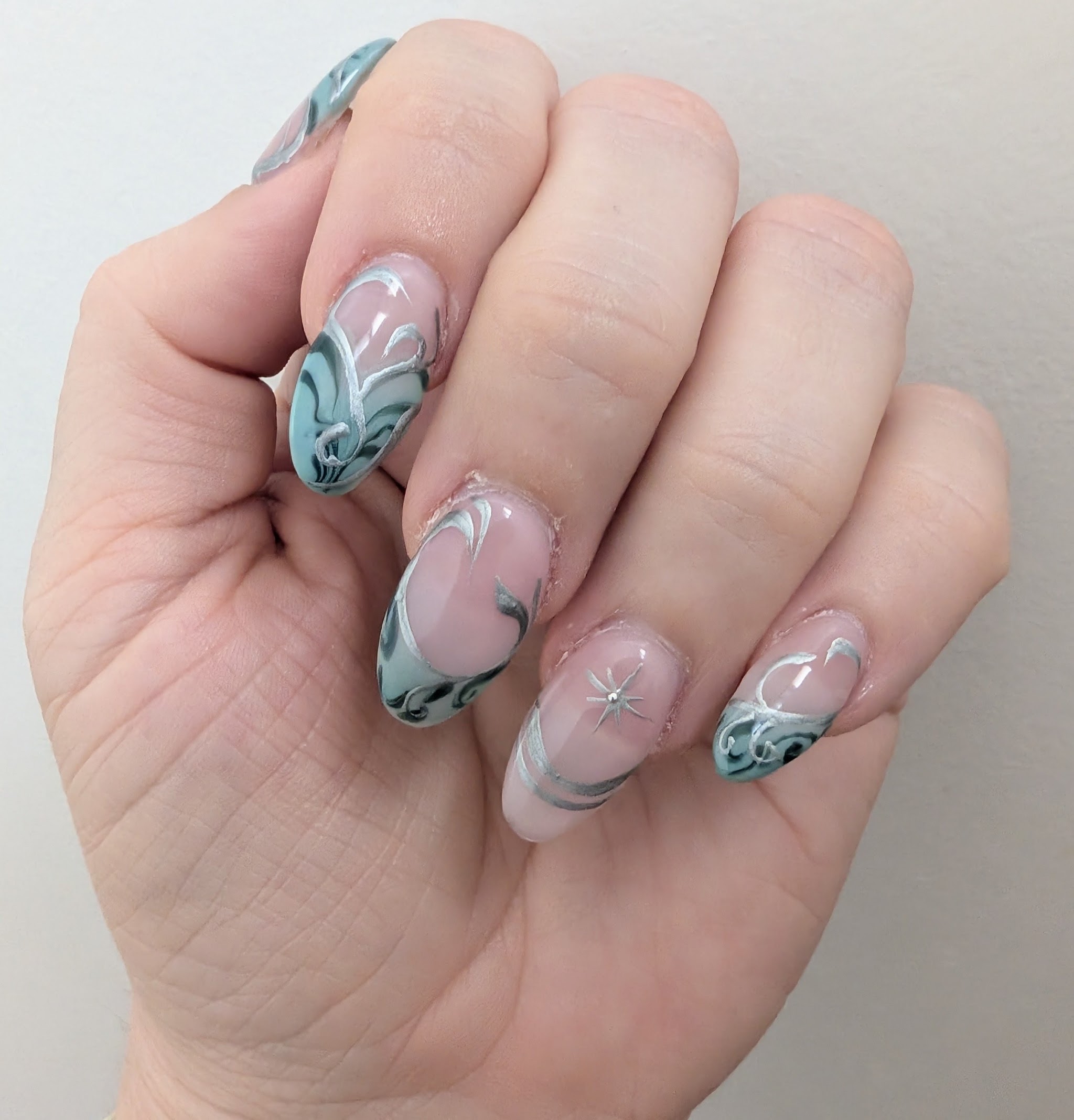 Pale teal marble swirl nails with silver line work and a starburst accent
